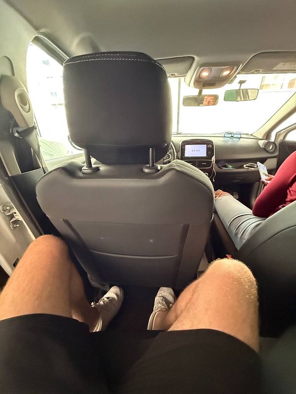 Inside a car, a view from the back seat shows a passenger's legs and the front dashboard.