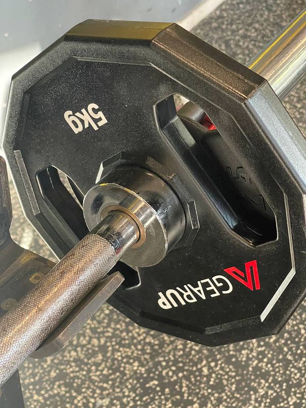 A close-up view of a weight plate attached to a barbell in a gym setting.