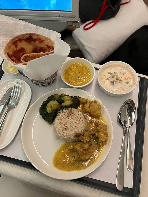An airplane meal featuring rice, chicken curry, vegetables, and various side dishes.