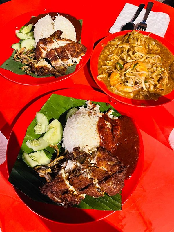 The image features a vibrant display of Malaysian dishes, including nasi lemak and a plate of noodles.
