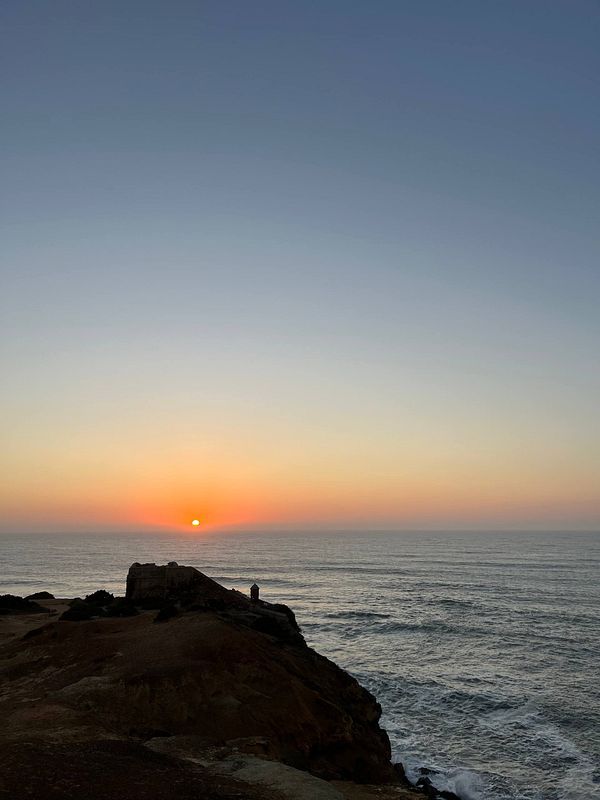A stunning sunset over the ocean viewed from a rocky cliff.