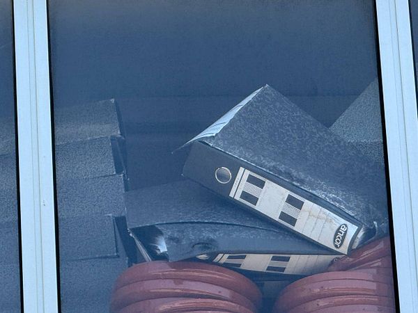 The image captures a stack of black binders and red weights behind a glass window.