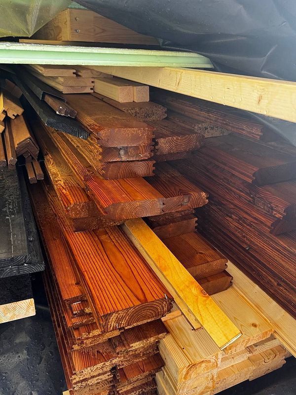 A stack of various wooden planks is shown, some of which are wet from rain.
