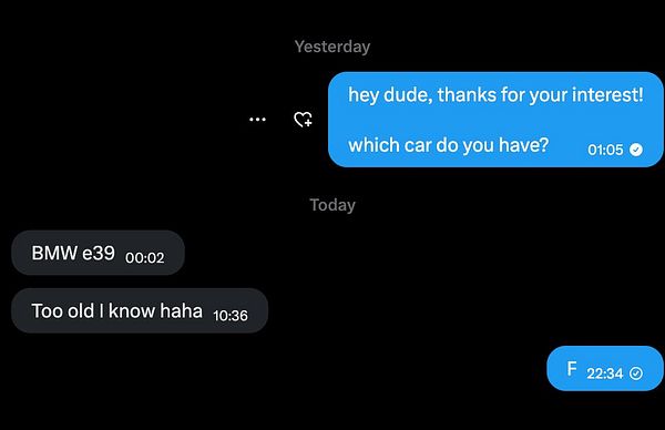 A silver BMW sedan with visible wear and modifications parked in a driveway with greenery in the background.