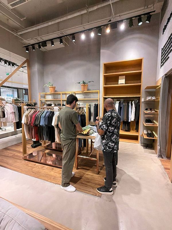 Photograph of a person sitting indoors wearing a beige linen outfit surrounded by plants and furniture.
