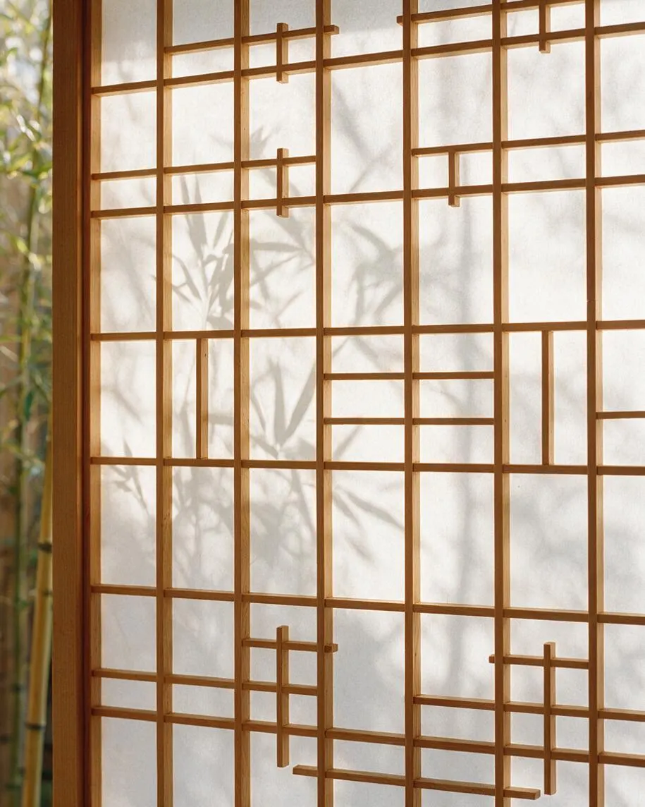 A close-up of a Japanese Zen-style shoji screen with a light wood lattice over translucent paper. Soft bamboo shadows fall across the panels, creating a calm, natural atmosphere with warm daylight filtering through.