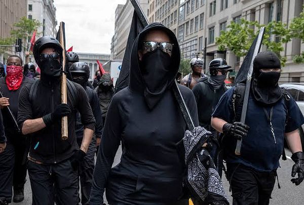 A group of individuals dressed in black attire participates in a protest.