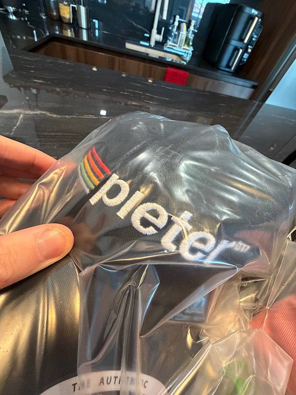 A hand is holding a cap with the brand name 'pieters' visible on it, packaged in plastic.