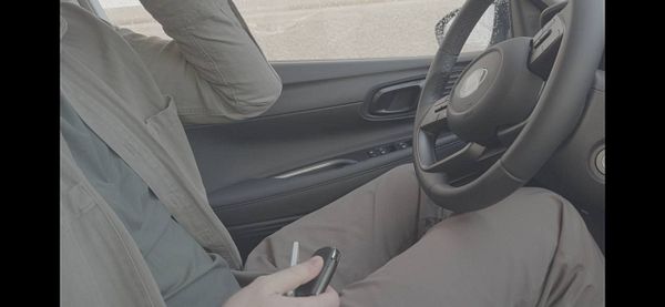 A person is seated in a car, holding a car key fob while looking thoughtful.