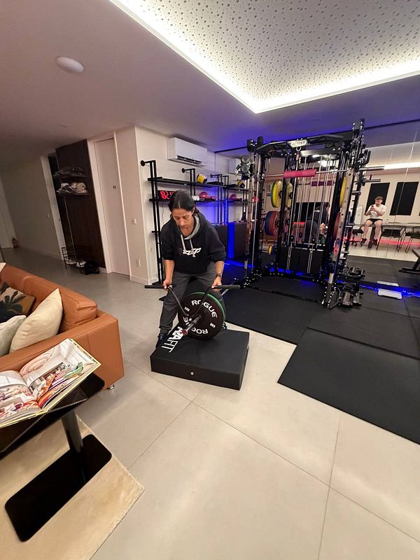 A cluttered gym locker room with benches, bags, and an open locker containing gym gear.