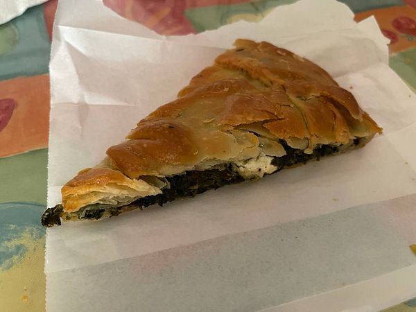 A slice of spanakotiropita is presented on a piece of white paper.