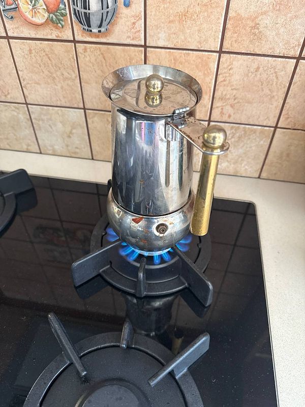 A moka pot is brewing coffee on a gas stove.