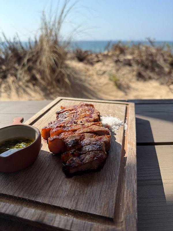 A beautifully presented dish of grilled meat on a wooden platter with a beach view in the background.
