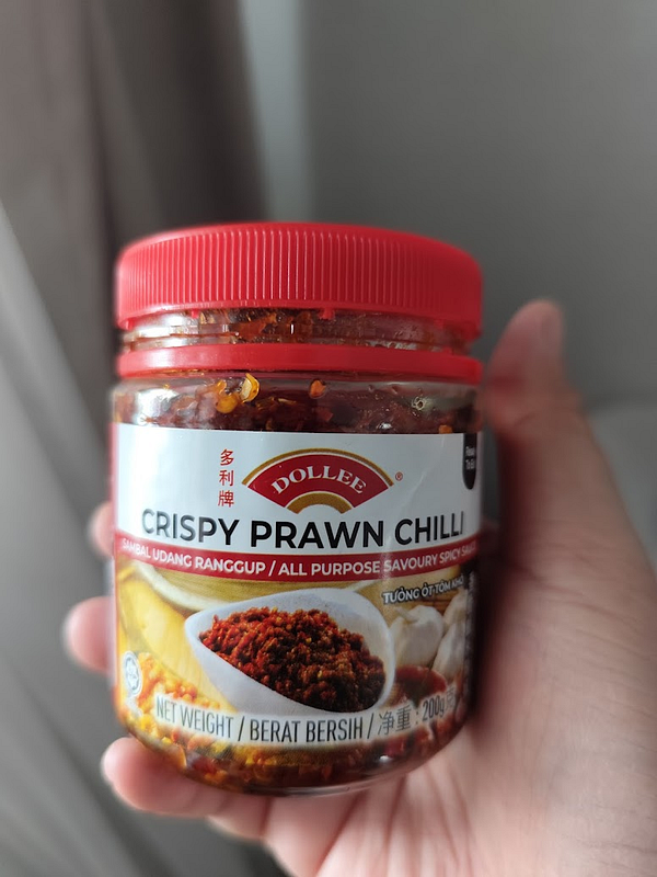 A jar of crispy prawn chili sauce is being held in a person's hand.