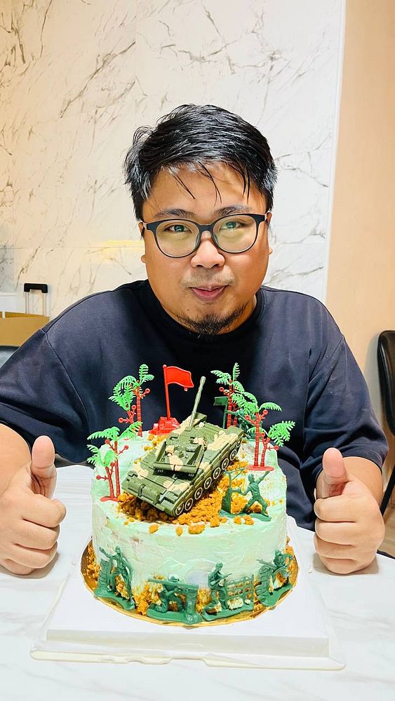 Image of a rectangular cake with a surprised face decoration, surrounded by colorful sprinkles and a black base.