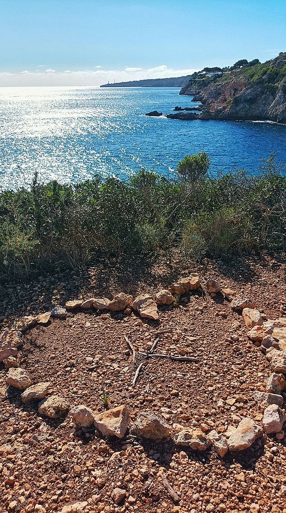 A heart-shaped arrangement of stones and twigs is set against a scenic coastal backdrop.