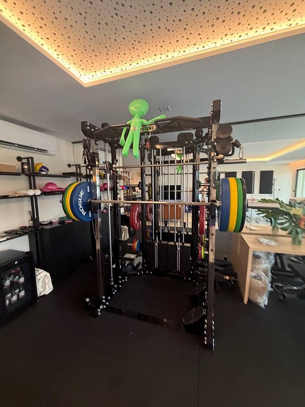 Man squats with a barbell loaded with weight plates inside a gym rack.
