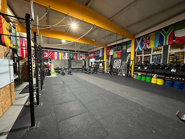 A spacious gym interior featuring various workout equipment and international flags.