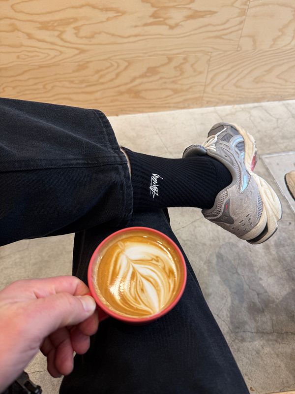 A hand holding a latte art coffee cup with a casual outfit in a café setting.
