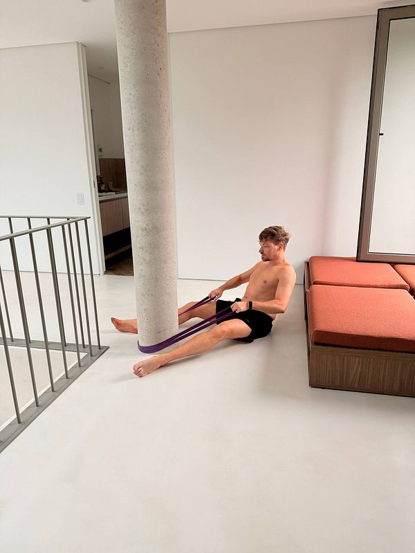 A young man wearing glasses and workout attire is exercising on a rowing machine in a gym.