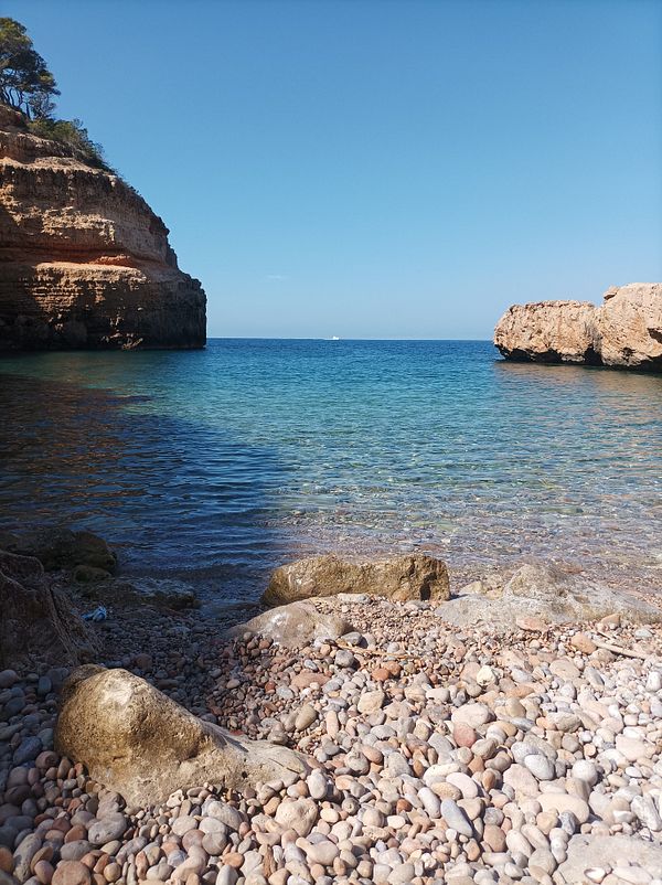 A serene beach scene featuring clear blue water and rocky shores.