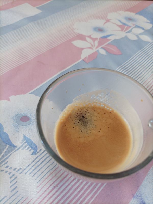 A close-up view of a glass of espresso on a patterned tablecloth.
