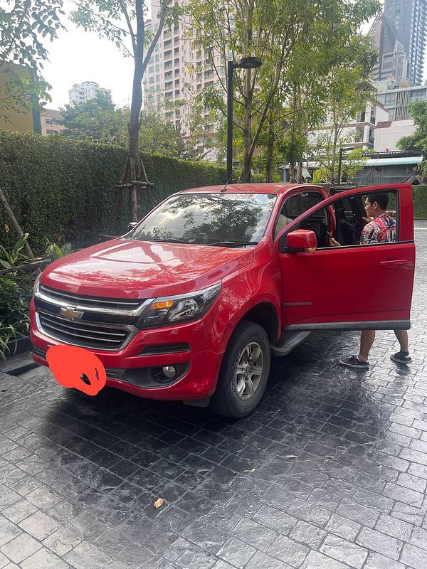 A red Chevrolet Colorado parked in a modern urban setting with a person preparing to load items.