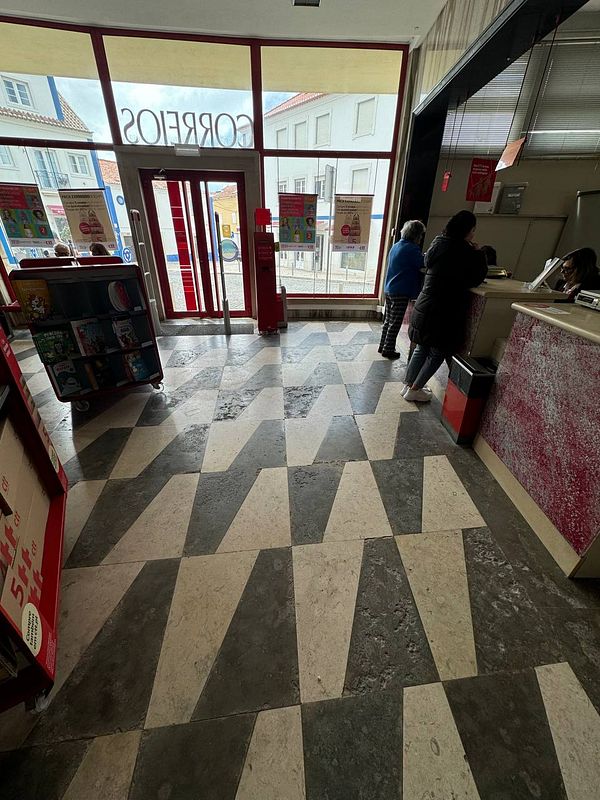 The image depicts the interior of a postal office with a distinctive floor pattern and several customers interacting with staff.