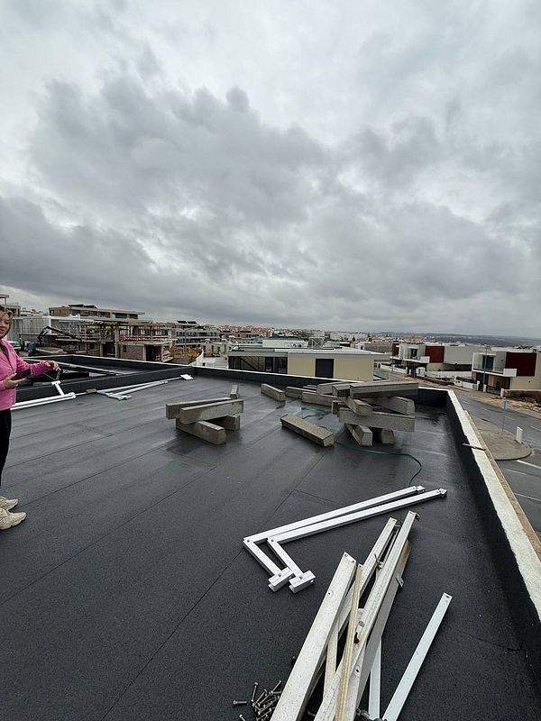 A rooftop scene showing uninstalled solar panel components and a person standing nearby.