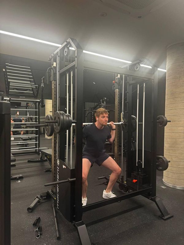 A person is performing squats with a barbell in a modern gym setting.