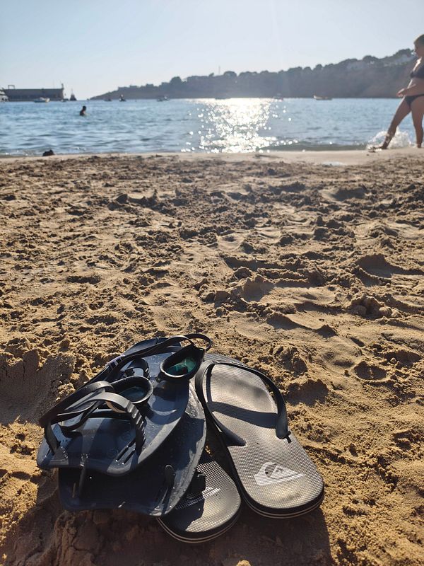 A photo of a sandy beach with people swimming and sunbathing near the shore, under a partly cloudy sky.
