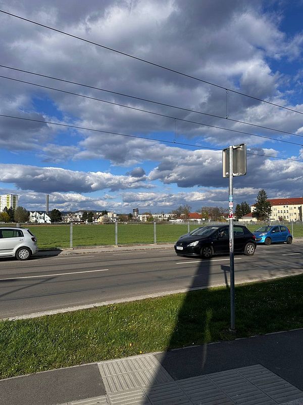 A view of a neighborhood with a grassy area, a road, and several cars parked along the street.