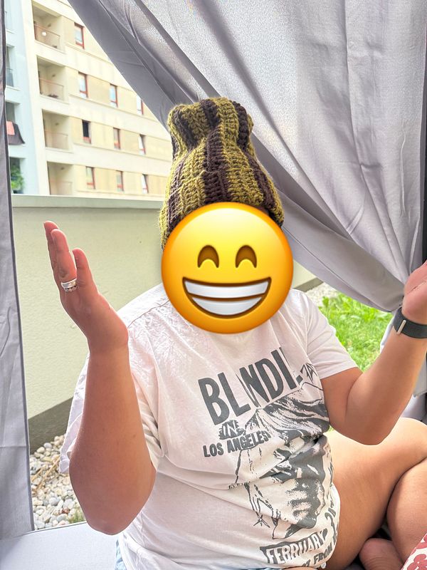 A person wearing a striped beanie is sitting outdoors, gesturing with their hands.