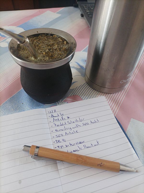 A workspace featuring a traditional mate drink, a notebook with a to-do list, and a thermos.