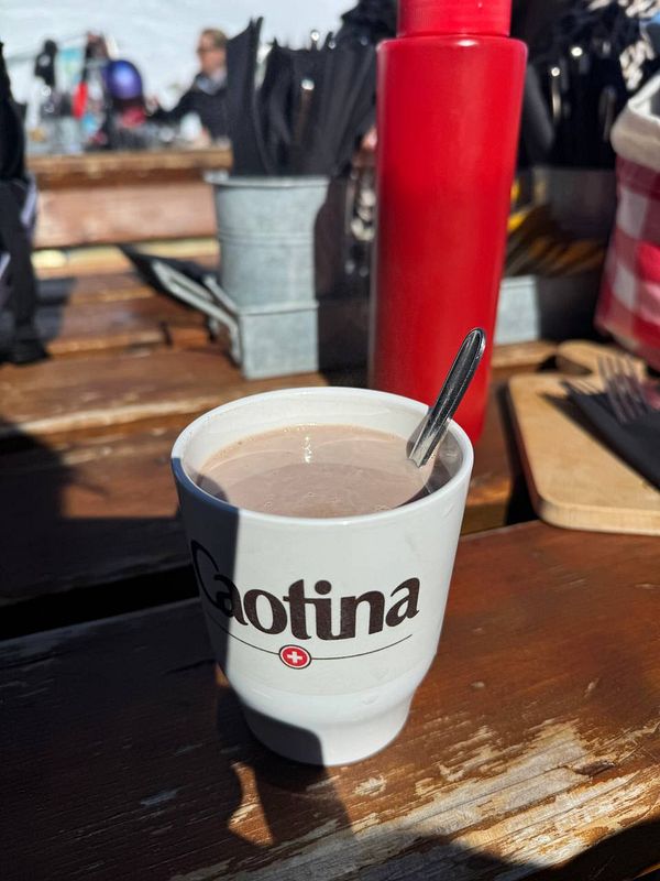 A cup of hot chocolate is placed on a wooden table in a ski resort setting.