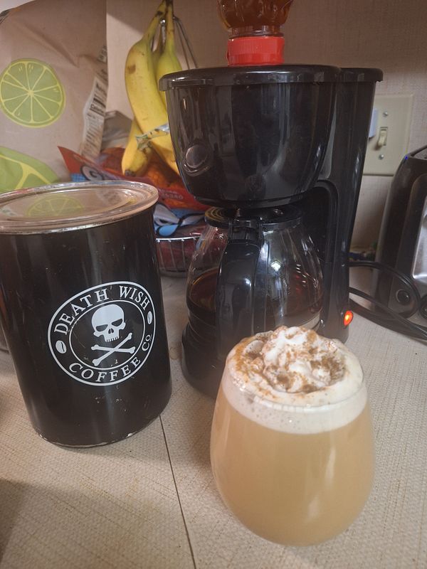 A coffee brewing setup with a fancy latte in a glass, surrounded by coffee supplies.