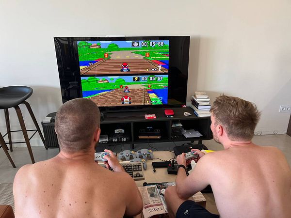 Two men are playing a video game on a large TV in a casual indoor setting.