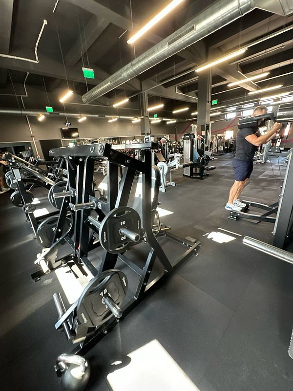 A well-equipped gym interior featuring various weightlifting machines and a person exercising.