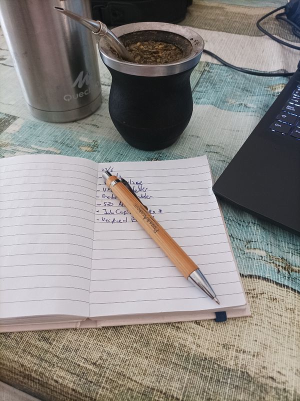 A workspace setup featuring a notebook, a pen, a mate cup, and a laptop.
