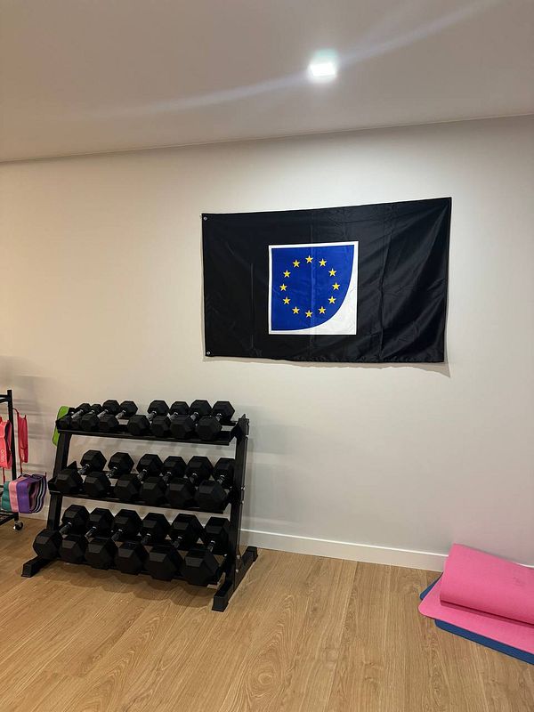 A home gym featuring a European Union flag on the wall and a rack of dumbbells.