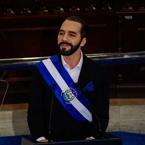 A man in formal attire delivers a speech while wearing a ceremonial sash.