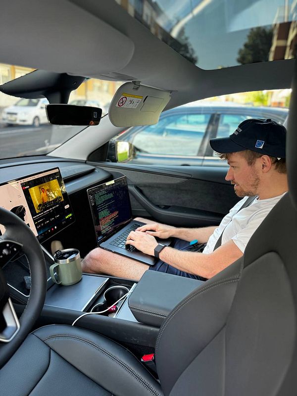 A person is working on a laptop inside a Tesla Model Y while enjoying a cup of coffee.