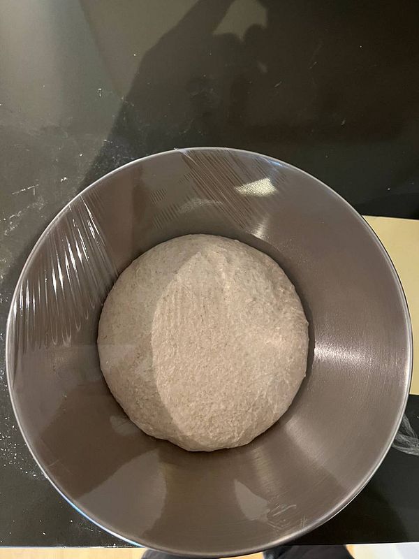 A bowl containing pizza dough covered with plastic wrap.