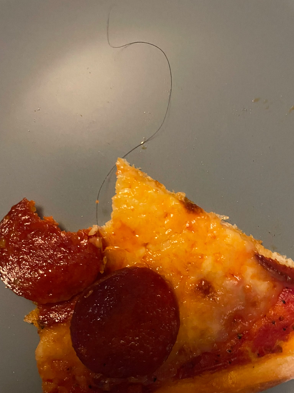 A slice of pepperoni pizza with a long hair on it, placed on a gray surface.