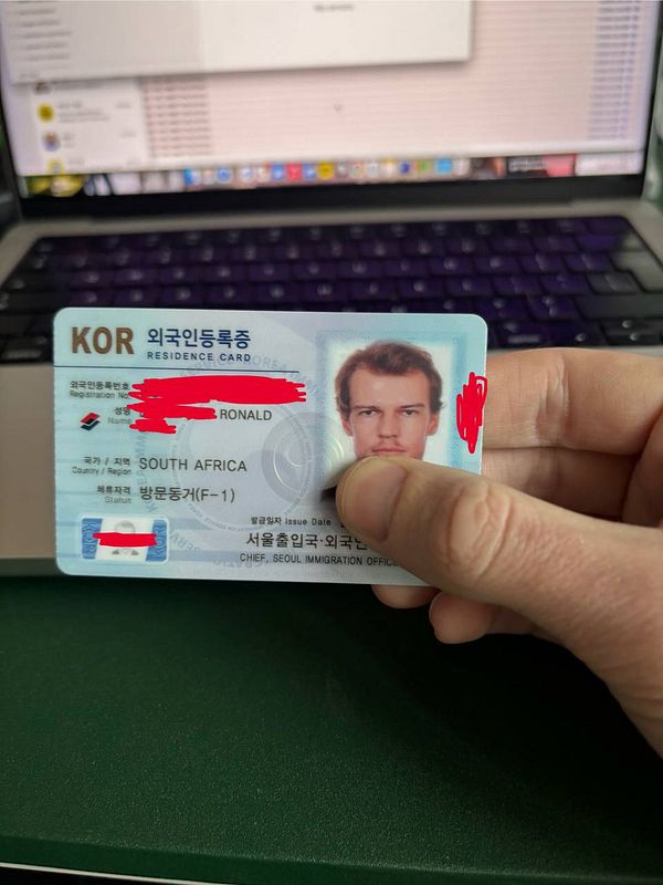 A residence card is being held in front of a laptop.