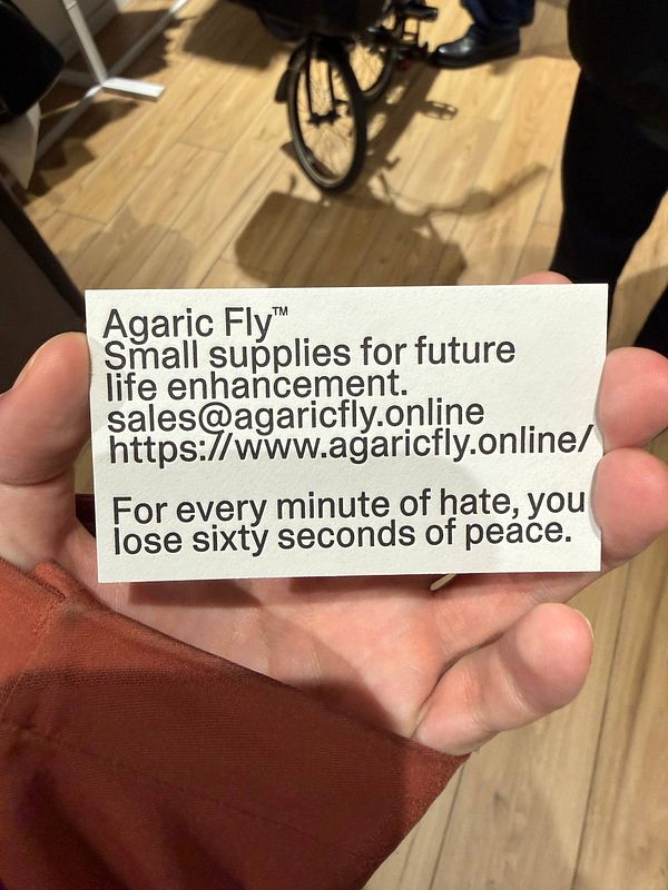 Fashion runway scene featuring a model walking in a colorful outfit with seated audience members on both sides.