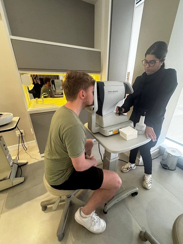 A young man is undergoing an eye checkup with a technician in a modern clinic.