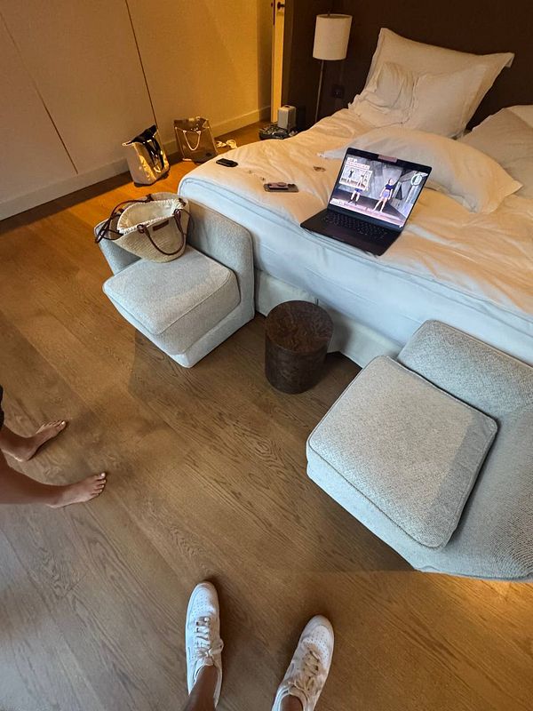 A hotel room with a bed, a laptop displaying a workout video, and personal items scattered around.