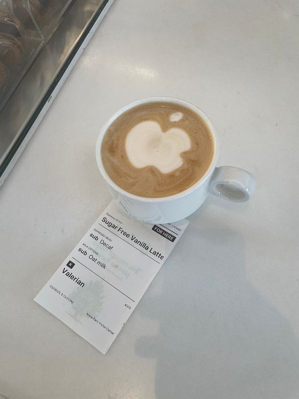 A coffee cup with an Apple logo design on the foam sits on a table next to a receipt.