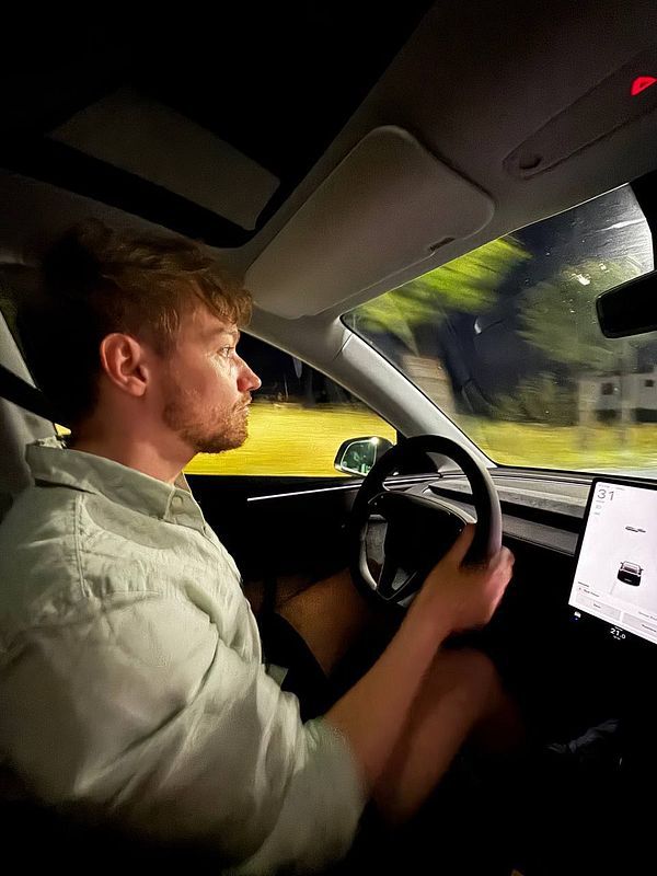 A person is driving a Tesla at night, focused on the road ahead.